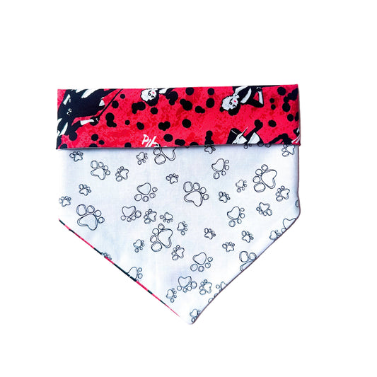 Dog bandana with red and black pattern on top and white with paw prints on bottom, on a white surface.
